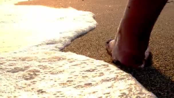 Piernas y pies femeninos caminando a lo largo de olas de agua de mar en la playa de arena. Salpicaduras de agua y espuma. Mujer pies caminando descalzo en playa de arena de mar. — Vídeos de Stock