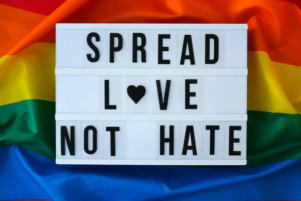 Tęczowa flaga ze światłem i tekstem SPREAD LOVE NOT HATE. Tęczowa flaga Igbtq wykonana z jedwabiu. Symbol miesiąca dumy LGBTQ. Równe prawa. Pokój i wolność — Zdjęcie stockowe