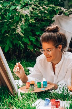 Bahçedeki sehpada ressam resmi. Açık hava sanat atölyesi. Parktaki bir piknik sırasında çimlerin üzerine fırça ve paletle resim çiz.