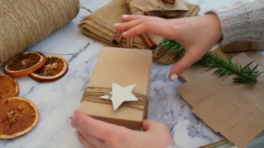 Yeni yıl hediyeleriyle dolu bir kutu hazırlayan kadın, el işi kağıdına sarılmış ve köknar dallarıyla süslenmiş. Tatiller ve Hediyeler konsepti. El yapımı çevre dostu alternatif yeşil Noel hediyeleri sıfır atık