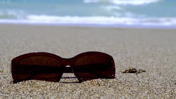 Lunettes de soleil sur le sable. Concept vacances d'été. Lunettes de soleil protectrices sur la plage de sable fin au bord de la mer tropicale par temps chaud et ensoleillé. — Video