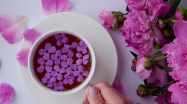Pembe şakayık çiçekli 4K yaratıcı düzen. Parlak masada bir fincan çay tutan kadın. Bahar mevsimi sevgililer günü, kadın, anne, 8 Mart bayramı, romantik kahvaltı. Tarz sahibi blog yazarı.