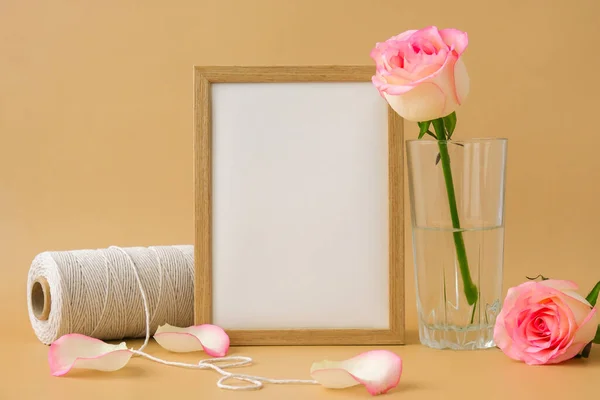 Moldura de madeira com papel branco vazio em branco e delicado carretel de rosas rosa de corda de algodão branco no fundo bege. Composição moderna mínima. Flores românticas rosa pastel. Terra neutra — Fotografia de Stock