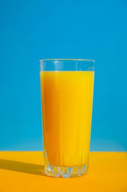 Mavi ve sarı arka planda bir bardak taze sıkılmış portakal suyu. Meyve suyu, taze soğuk içecek. Yazın dinlenmek için. Boşluğu kopyala