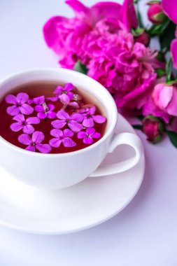 Pembe şakayık çiçekleri ve parlak masa üzerinde bir fincan çayla yaratıcı bir düzen. Bahar mevsimi sevgililer günü, kadın, anne, 8 Mart bayramı, romantik kahvaltı. Şık bir blog yazarı. Tebrik kartı. Davetiye. Günlük postası