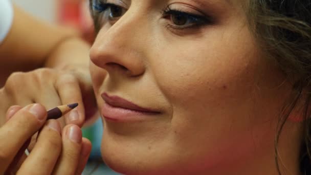 Make up artist applying lipstick. close-up of the lips of a young woman, professional makeup artist with a brush applies natural color lipstick. fashion backstage. — Stock Video