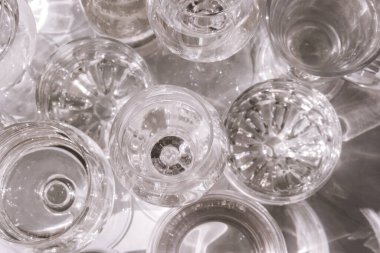 Güneş ışığında beyaz arka planda duran farklı güzel gözlükler gölgeler yaratır. Sert ışık, uzun gölgeler. Yaratıcı içki konsepti, alkol kokteyli. Cam kaplama konsepti. Geometrik şekiller