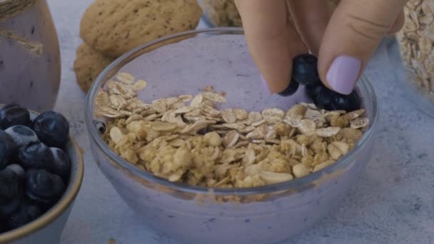 Mulher preparando Saudável tigela de smoothie de mirtilo com mirtilos, sementes de chia e granola. Café da manhã vegetariano vegan saudável. Nutrição e dieta. — Vídeo de Stock