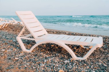 Denizin önündeki boş güneş pansiyonları. Kumsalda güneş sandalyeleri. Büyük dalgalar fırtınalı hava. Denizin kenarında boş bir şezlong ve katlanmış şemsiye standı. Yaz tatili