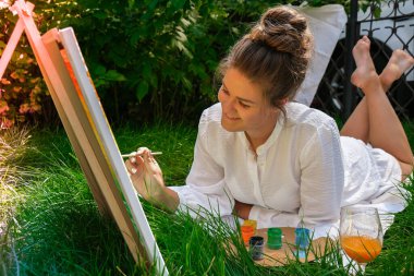 Bahçedeki sehpada ressam resmi. Açık hava sanat atölyesi. Parktaki bir piknik sırasında çimlerin üzerine fırça ve paletle resim çiz.