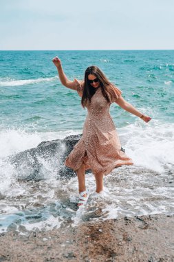 Plajda gökyüzüne karşı poz verirken giyinen ve su sıçratan bir kadın. Deniz manzaralı. Yaz tatili konsepti