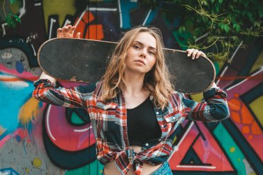 Renkli sokak sanatında kaykay süren bir kadın. Uzun kaykaylı kaykaycı kız. Gün batımında havalı bir bayan kaykaycı. Kaygısız kadın patenci 20 'li yaşlarda özgürlüğün tadını çıkarıyor gençlik hobisi