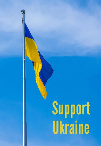 APOYO UCRANIA texto sobre bandera nacional de Ucrania ondea en el viento contra el cielo azul. El símbolo nacional de los ucranianos - azul y amarillo. No hay guerra. Protesta de guerra contra la invasión rusa de —  Fotos de Stock
