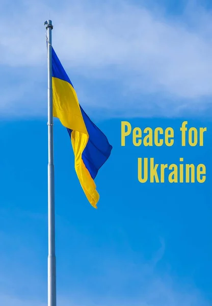 FRIEDEN FÜR UKRAINE Text auf der ukrainischen Nationalflagge flattert im Wind gegen den blauen Himmel. Nationales Symbol des ukrainischen Volkes - blau und gelb. Kein Krieg. Kriegsprotest gegen russische Invasion — Stockfoto