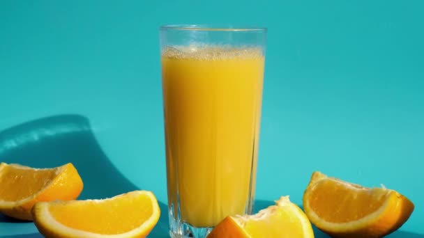 Main féminine mettre et prendre un verre de jus d'orange frais pressant avec des fruits tranchés sur fond bleu. Jus de fruits, boisson fraîche et fraîche. Rafraîchissements en été. Fruits coupés en deux — Video