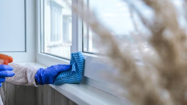 Pencerenin pervazını temizliyorum cam parmaklıkları temizlemek için mavi mikrofiber bezle toz temizliyorum Mavi Eldiven Spreyli Sıvı kullanıyorum. Ev işi ve temizlik konsepti. Genel Bahar Temizliği