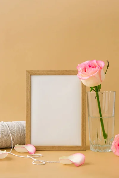 Moldura de madeira com papel branco vazio em branco e delicado carretel de rosas rosa de corda de algodão branco no fundo bege. Composição moderna mínima. Flores românticas rosa pastel. Terra neutra — Fotografia de Stock