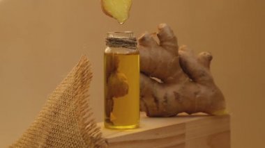 Esaslı zencefil yağı damlayan cam şişe, bej arka planda zencefil kökü. Sağlıklı alternatif yaşam. Zingiber officinale Cilt bakımı, vücut ve saç bakımı için doğal kozmetik malzemeleri