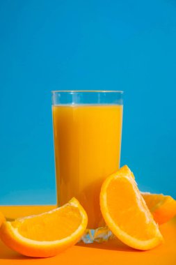 Mavi ve sarı arka planda dilimlenmiş meyveli taze sıkılmış portakal suyu. Meyve suyu, taze soğuk içecek. Yazın dinlenmek için. Meyveler yarı yarıya kesilmiş Boşluğu kopyala