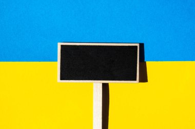 Kağıttan yapılmış Ukrayna bayrağına karşı siyah karatahta yazılı tahta etiket. Metnin için şablon oluştur. Savaşı durdurun. Ukrayna 'daki savaşı bitirme kavramı. Ulusal sembol - mavi ve sarı. Sancak boyutu Boşluğu kopyala