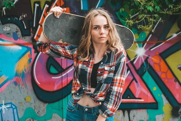 Mujer montando un monopatín en colorido arte callejero. Chica patinadora en un longboard. Patinadora femenina genial al atardecer. Patinadora femenina despreocupada años 20 disfrutando de la libertad estilo de vida juvenil Hobby —  Fotos de Stock