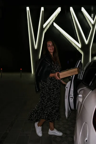 Тусуюсь. Молодая небрежная женщина на парковке ест пиццу по ночам. Миллениальное поколение поколения генов z — стоковое фото