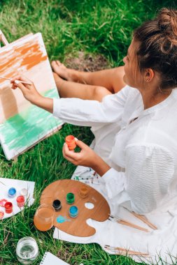 Bahçedeki sehpada ressam resmi. Açık hava sanat atölyesi. Parktaki bir piknik sırasında çimlerin üzerine fırça ve paletle resim çiz.
