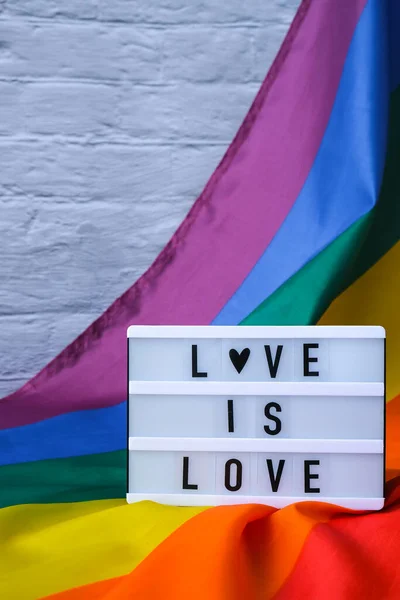 Tęczowa flaga ze światłem i tekstem LOVE IS LOVE. Tęczowa flaga Igbtq wykonana z jedwabiu. Symbol miesiąca dumy LGBTQ. Równe prawa. Pokój i wolność — Zdjęcie stockowe