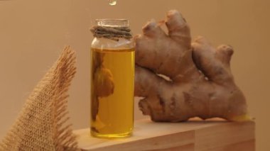 Esaslı zencefil yağı damlayan cam şişe, bej arka planda zencefil kökü. Sağlıklı alternatif yaşam. Zingiber officinale Cilt bakımı, vücut ve saç bakımı için doğal kozmetik malzemeleri