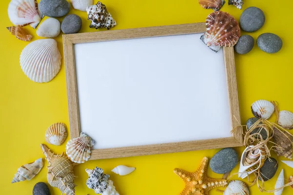 Fotokopi alanı, deniz kabukları, çakıl taşları, sarı arka plan için kompozisyon çerçevesi. Boşluk, üst görünüm, durgun hayat, düzlük. Deniz seyahati konsepti turizm ve tatil beldeleri. Yaz tatili