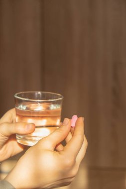 Female hand holding glass of water and pink pill. Collagen supplement for nutrition. Healthy eating lifestyle. Taking vitamins or nutritional supplements. Preventive medicine. Healthcare and wellbeing