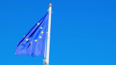 EU European flag poole blowing in the wind on a bright sunny summers day. Frayed European Union flag is fluttered by strong wind, blue sky background