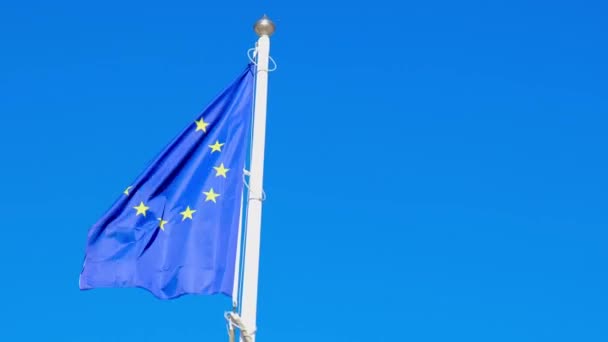 Poole de la bandera europea de la UE que sopla en el viento en un día soleado brillante de los veranos. Bandera de la Unión Europea deshilachada es ondeada por el viento fuerte, fondo cielo azul — Vídeos de Stock