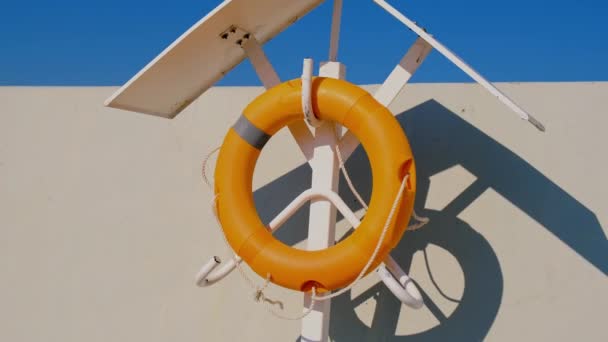 Orange lifebuoy on beach by sea. Safety equipment for rescuing people on seashore. Orange lifebuoy on the pier of blue sky and azure sea — ストック動画