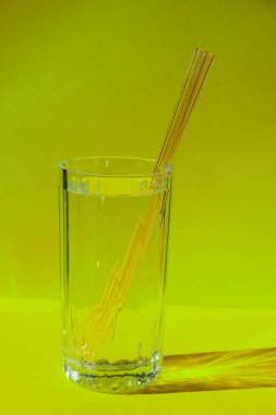 Reusable glass Straws in Glass with water on yellow background Eco-Friendly Drinking Straw Set with cleaning brush. Zero waste, plastic free concept