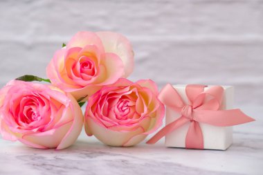 Pembe arka planda bağlı kurdeleli pembe güllü hediye kutusu. Tebrik kartı. Bahar tatilleri için mevcut Metin için alanı kopyala.