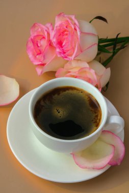 Vazoda pembe bir gül ve bej arka planda beyaz bir fincan kahve. Minimum bileşim. Romantik pastel pembe gül çiçeği. Modern estetik. Tarafsız toprak tonları. Tatil sabahı kahvaltısı