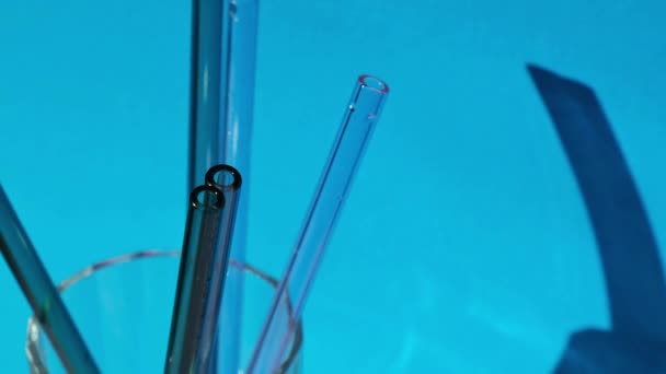 Reusable glass Straws in Glass with water on blue background Eco-Friendly Drinking Straw Set with cleaning brush. Zero waste, plastic free concept — Vídeo de Stock