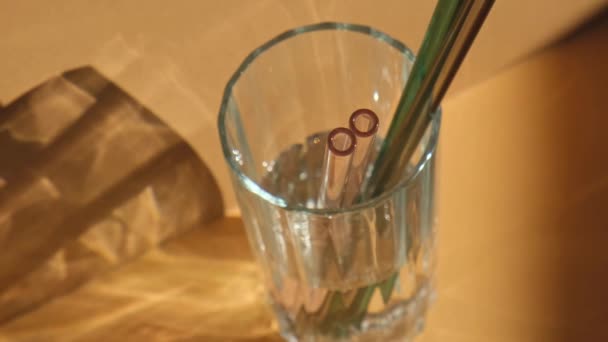 Herbruikbare glazen rietjes in glas met water op beige neutrale ondergrond Eco-Friendly Drinking Rietje Set met reinigingsborstel. Geen afval, kunststofvrij concept — Stockvideo