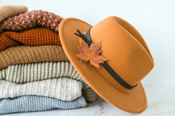 Stack of cozy knitted warm sweater with Autumn fall maple leaf and beige stylish hat. Sweaters in retro Style. Orange and blue colors. Cozy hygge concept Copy space Autumn season