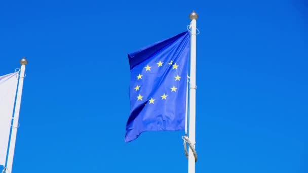 Bandera europea de la UE con poole de bandera nacional de Polonia soplando en el viento en un día soleado de veranos brillantes. Bandera de la Unión Europea deshilachada es ondeada por el viento fuerte, fondo cielo azul — Vídeo de stock