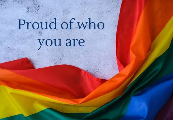 Regenbogenfahne mit Text PROUD OF WHO YOU SIND message. Regenbogen lgbtq Flagge aus Seidenmaterial. Symbolmonat des LGBTQ-Stolzes. Gleiche Rechte — Stockfoto