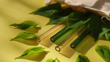 Renkli arka planda yeniden kullanılabilir cam pipetler, çevre çantasında yeşil yapraklar, çevre dostu içici pipetler, yeniden kullanılabilir konforlu yuvarlak uçlu pipet içme. Sıfır atık, plastiksiz konsept. Piknik