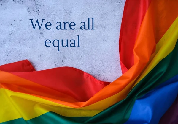 Gökkuşağı bayrağı ve metin Hepimiz Eşitiz mesajı. İpek kumaştan yapılmış gökkuşağı lgbtq bayrağı. LGBTQ gurur ayının sembolü. Eşit haklar — Stok fotoğraf