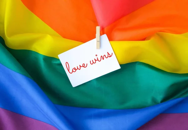 Tęczowa flaga z tekstem LOVE WINS wiadomość na papierze. Tęczowa flaga Igbtq wykonana z jedwabiu. Symbol miesiąca dumy LGBTQ. Równe prawa. — Zdjęcie stockowe