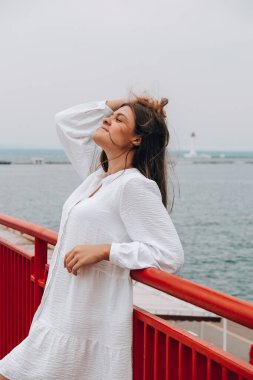 Deniz kıyısında mutlu bir kız, köprüde duruyor, gülümsüyor. Özgürlük için. Rüzgar kızın saçlarını savuruyor. Tatil konsepti. Hareketli bir yolculuk. Genç gezgin.