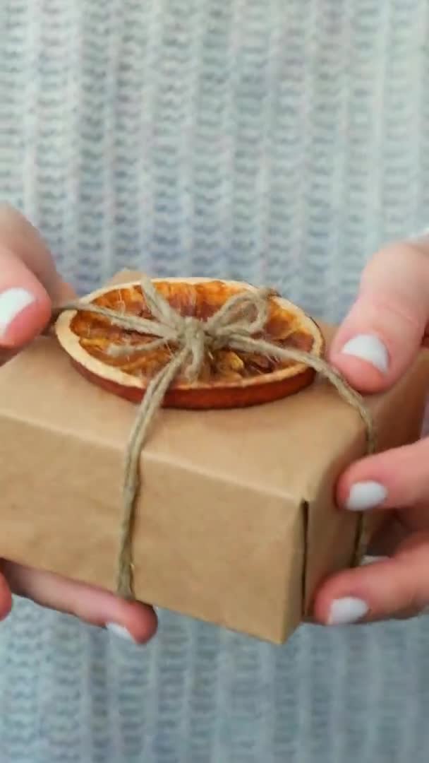 Mujer dando caja con regalos de Año Nuevo, envuelta en papel artesanal y decorada con rebanadas de naranja seca. Concepto de vacaciones y regalos. Eco hecho a mano alternativa verde Navidad presenta cero residuos — Vídeos de Stock