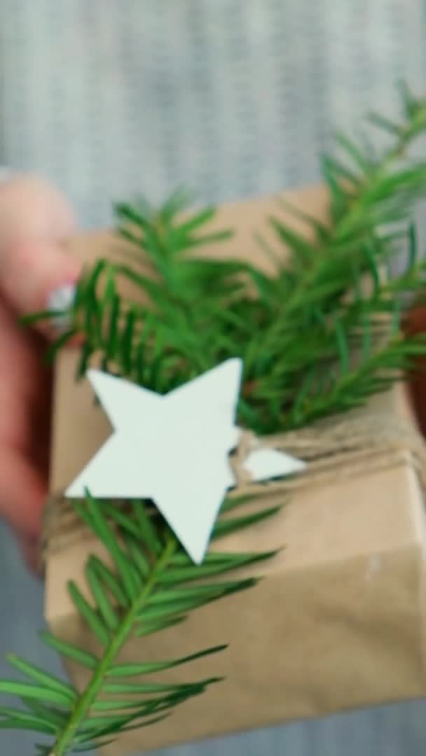 Kvinna ger Box med nyårspresenter, insvept i hantverkspapper och dekorerad med gran gren. Semester och gåvor koncept. Handgjort Miljövänligt alternativ grön jul presenterar noll avfall Vertikal — Stockvideo