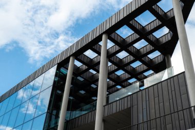 Gökyüzü arka planında cam cepheli modern ofis binası. Ofis binasının cam duvarında bulutların yansıması var. Modern Avrupa binasının dış cephesi