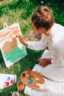 Bahçedeki sehpada ressam resmi. Açık hava sanat atölyesi. Parktaki bir piknik sırasında çimlerin üzerine fırça ve paletle çadır çiz. Yaratıcılık, sanat ve hobi